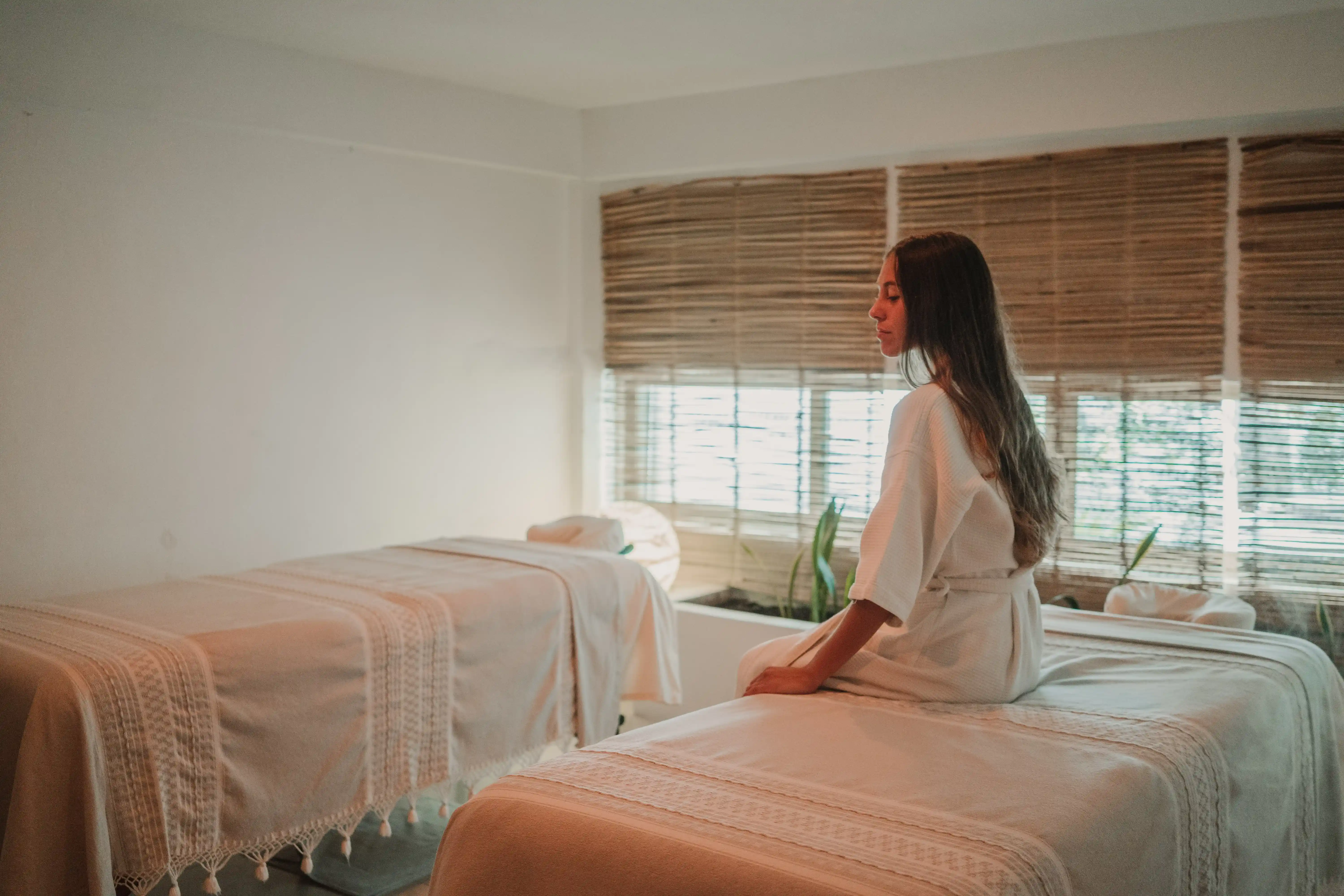 Woman in a white robe resting on a bed before an at-home massage