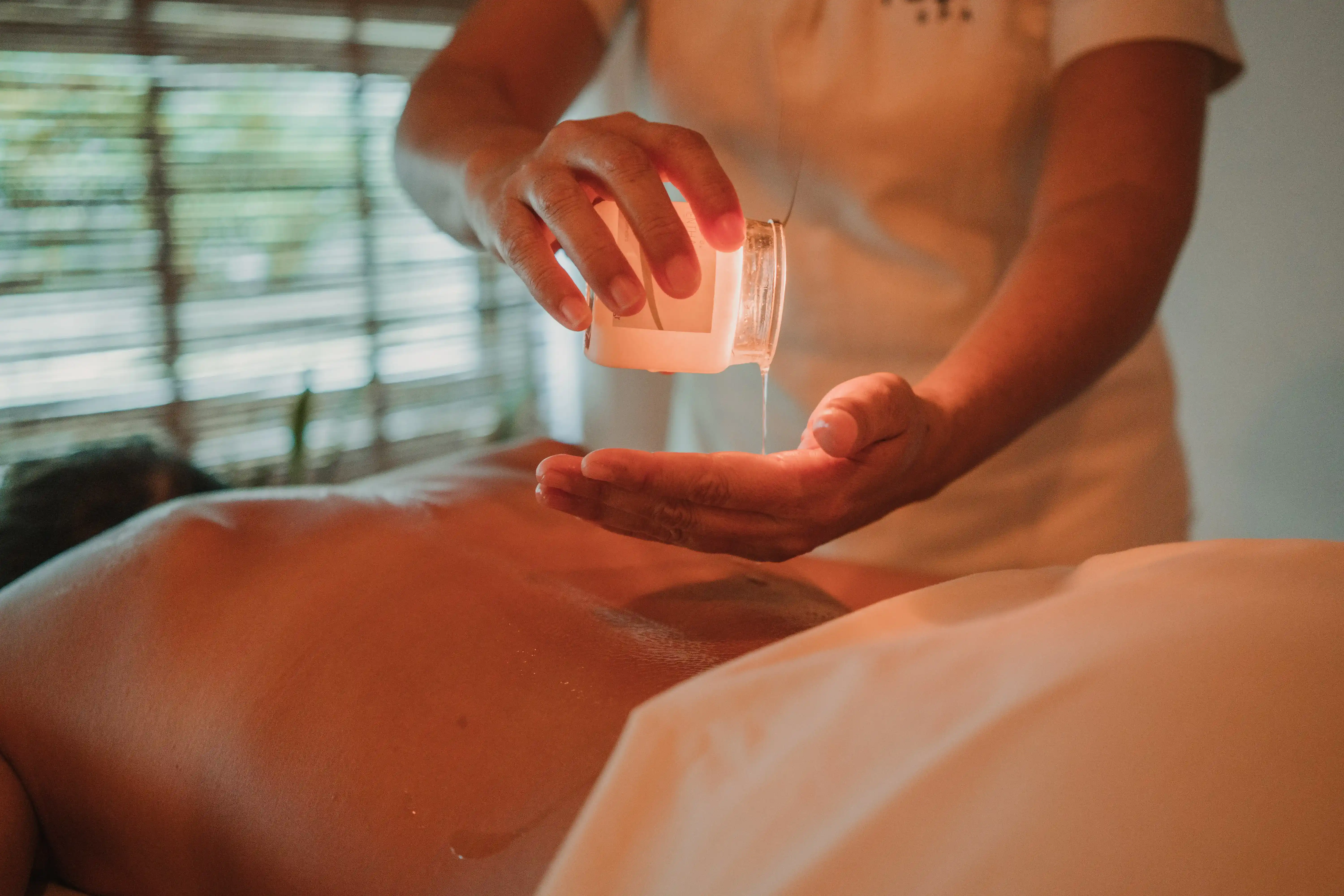 Therapist’s hands massaging a guest’s neck with warm oil